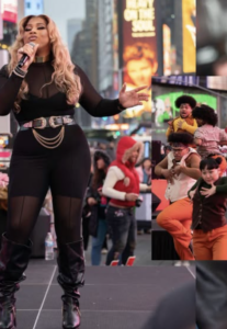 A woman sings on an outdoor stage in an urban area, celebrating LGBTQ pride, while a group of people dance energetically in a separate inset photo.